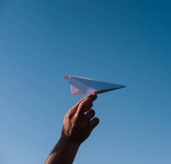 Holding a paper airplane in your hand against the blue sky. The art of origami. White paper airplane.
