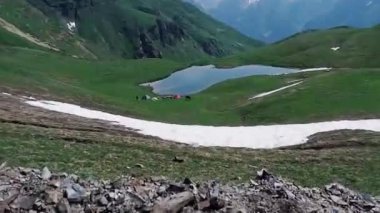 Gezginler bir dağ gölünün kıyısındaki çadırların yanında otururlar ve atlar yakınlarda yürürler. Georgia Dağları, Svaneti. Aktif eğlence ve popüler turizm merkezleri.