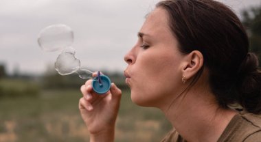 Kız sabun köpüğü üflüyor. Genç bir kadın doğada oturur ve sabun toplarını emer. Yüz profili, kenar görünüm.