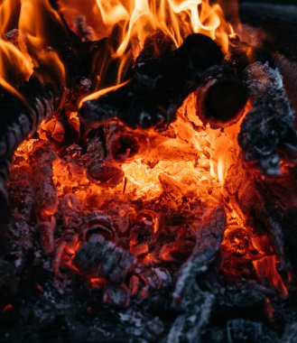 Ateşin parlak kırmızı alevleri. Kül ve kömür. Karanlık bir arka planda alevler. Sıcak kömür, barbekü yeri. Ateşin yanında açık hava eğlencesi..