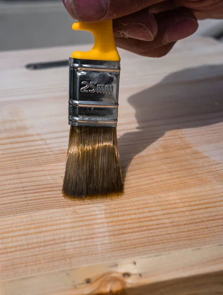 Open wood with varnish using a paint brush. Brush on a wooden table, fence, or floor. Open the work surface with varnish. Wood texture. To treat the wood with varnish.