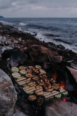 Izgaranın üzerinde ızgara yapılmış çeşitli sebze ve mantarlar. Sahildeki ateşte vejetaryen barbeküsü. Etsiz lezzetli ve sağlıklı yiyecekler..