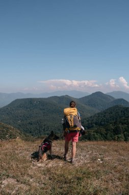 Bir kız gezgin ve Alman çoban köpeği bir tepede durup etraftaki dağlara bakıyorlar. Bir köpek gezgini ve sırt çantalı insan sahibi ulusal parkta yürüyor ve doğanın tadını çıkarıyorlar..
