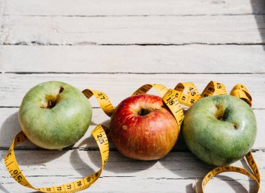 Beyaz ahşap arka planda üç elma sarısı, yeşil ve kırmızı ve sarı esnek kurdele. Lezzetli ve sağlıklı yiyecekler mutfak masasında..