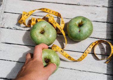 Bir insan yeşil taze elmalara ve üzerinde numaralar olan sarı bir kurdeleye dokunur. Sağlıklı ve zindelik için vitaminli lezzetli ve sağlıklı yiyecekler..