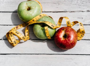 Beyaz ahşap arka planda üç elma sarısı, yeşil ve kırmızı ve sarı esnek kurdele. Lezzetli ve sağlıklı yiyecekler mutfak masasında..