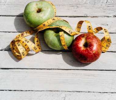 Beyaz ahşap arka planda üç elma sarısı, yeşil ve kırmızı ve sarı esnek kurdele. Lezzetli ve sağlıklı yiyecekler mutfak masasında..