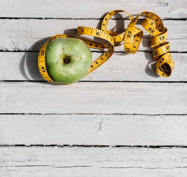 Esnek sarı bir banda sarılı yeşil bir Apple beyaz bir ahşap masanın üzerinde yatıyor. Fitness ve sağlıklı yaşam tarzı. Lezzetli ve sağlıklı yiyecekler, vitaminler ve mineraller.