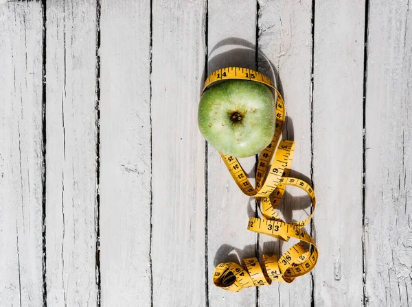 Esnek sarı bir banda sarılı yeşil bir Apple beyaz bir ahşap masanın üzerinde yatıyor. Fitness ve sağlıklı yaşam tarzı. Lezzetli ve sağlıklı yiyecekler, vitaminler ve mineraller.