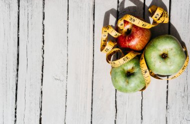 Beyaz ahşap arka planda üç elma sarısı, yeşil ve kırmızı ve sarı esnek kurdele. Lezzetli ve sağlıklı yiyecekler mutfak masasında..