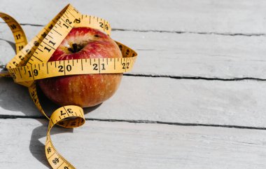 Esnek sarı bir banda sarılı kırmızı bir Apple beyaz bir ahşap masanın üzerinde yatıyor. Fitness ve sağlıklı yaşam tarzı. 2021 rakamlarıyla beslen.