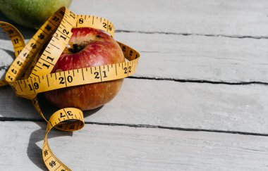 Esnek sarı bir banda sarılı kırmızı bir Apple beyaz bir ahşap masanın üzerinde yatıyor. Fitness ve sağlıklı yaşam tarzı. 2021 rakamlarıyla beslen.