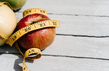 Esnek sarı bir banda sarılı kırmızı bir Apple beyaz bir ahşap masanın üzerinde yatıyor. Fitness ve sağlıklı yaşam tarzı. 2021 rakamlarıyla beslen.