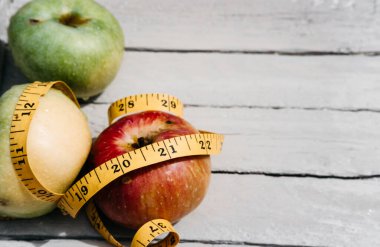 Kırmızı Elma esnek sarı bir banda sarılı beyaz bir ahşap masanın üzerinde yatıyor. Fitness ve sağlıklı yaşam tarzı. 2021 rakamlarıyla beslen.