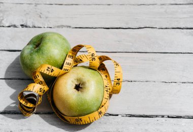 İki sarı ve yeşil elma beyaz ahşap bir masanın üzerinde yatıyor ve sarı bir bant ile sarılmış. Fitness ve sağlıklı yaşam tarzı. Vitaminler ve mineraller, lezzetli ve sağlıklı yiyecekler..