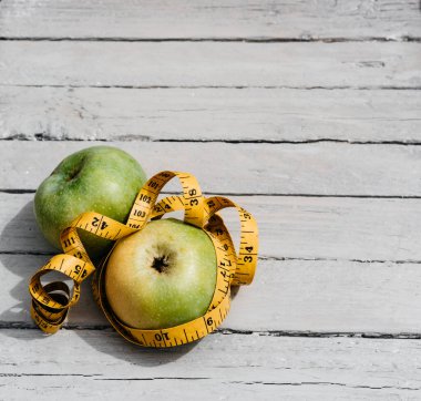 İki sarı ve yeşil elma beyaz ahşap bir masanın üzerinde yatıyor ve sarı bir bant ile sarılmış. Fitness ve sağlıklı yaşam tarzı. Vitaminler ve mineraller, lezzetli ve sağlıklı yiyecekler..