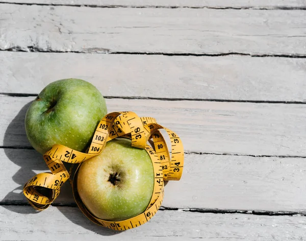 两个黄色和绿色的苹果躺在一个白色的木制桌子上 用一根黄色的厘米带子包裹着 健康和健康的生活方式 维生素和矿物质 美味和健康食品 — 图库照片