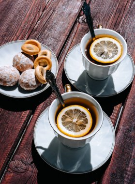 Ahşap bir masada limonlu iki fincan siyah çay ve lezzetli simit ve çay tabağında zencefilli ekmek. Çay içmek için güzel beyaz seramik sofra takımı.