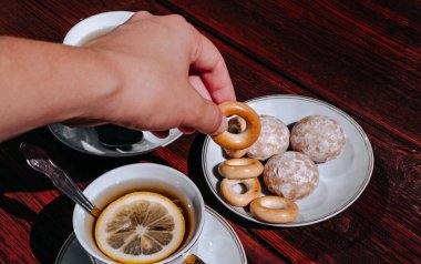 Güzel beyaz bir kasede limonlu siyah çay ve şekerle ahşap bir masada duruyor. Elinde taze pişmiş tatlı bir simit tut..