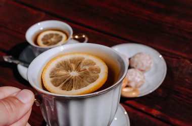 Elinde limonla bir fincan çay tut. Lezzetli yemek ve şekerli çay partisi. Seramik beyaz kupa ve çay takımı.