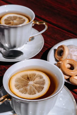 Ahşap bir masada limonlu iki fincan siyah çay ve lezzetli simit ve çay tabağında zencefilli ekmek. Çay içmek için güzel beyaz seramik sofra takımı.