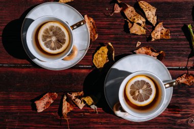 Ağaçlardan dökülen sarı sonbahar yapraklarının yanında, ahşap bir masada seramik çay seti. Limonlu ve şekerli siyah çay, iki kişilik çay töreni..