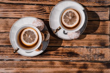 İki beyaz seramik çay fincanı ahşap bir masada çay tabağı üzerinde. Limonlu ve şekerli siyah çay. İki kişilik çay seremonisi için çok güzel bir mutfak..