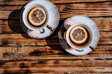 İki beyaz seramik çay fincanı ahşap bir masada çay tabağı üzerinde. Limonlu ve şekerli siyah çay. İki kişilik çay seremonisi için çok güzel bir mutfak..