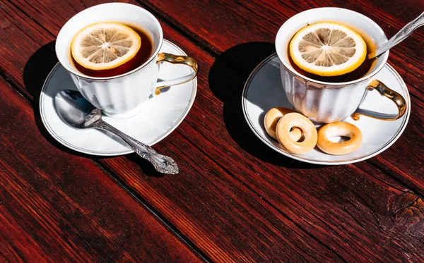 Two white cups of tea and lemon are placed on a mahogany wooden table. The tea party and a good time. Drink tea with bagels.