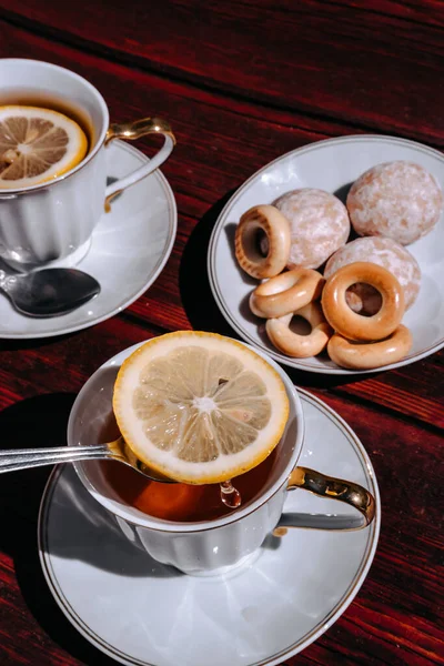 Black tea with lemon and sweets in a beautiful white bowl stands on a wooden table. Stir the water in the tea with a small teaspoon and add the sugar.