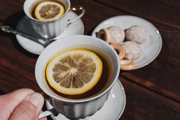 Hold a Cup of tea with lemon in your hand. Tea party with delicious food and sweets. Ceramic white Cup and tea set.