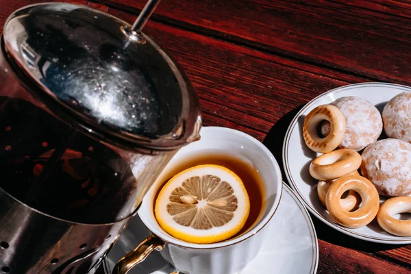 stock image Pour tea from a teapot into a beautiful white ceramic Cup with a gold handle. Sweets for tea in a white saucer, a beautiful tea set for the tea ceremony.