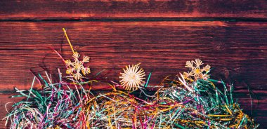 Noel renkli, parlak yağmur ve kahverengi ahşap bir masada saman Noel oyuncakları. Noel süsleri, parlak renkli süsler. Yatay formatta güzel bir Noel ağacı arkaplanı.