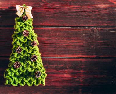 Çam kozalakları ve kafasının üstünde altın bir fiyonk bulunan el yapımı yeşil bir Noel ağacı kahverengi bir ahşap arka planda yatar. Güzel yeni yıl afişi. Mutlu yıllar ve mutlu Noeller..