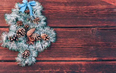 Noel ağacı şeklinde parlak yeşil bir süs koni ve ahşap arka planda mavi bir fiyonk. Güzel bir Noel geçmişi. Mutlu yıllar ve mutlu Noeller..