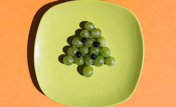 绿色葡萄圣诞树 绿色盘子上装饰着蓝色葡萄 一个美丽的 轻盈的和美味的圣诞小吃为全家 为新年的自助餐请客的想法 — 图库照片