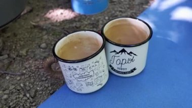İki beyaz kamp bardağına sıcak siyah çay dök. Kampta canlandırıcı bir sıcak içecek, temiz hava ve çay seremonisi..