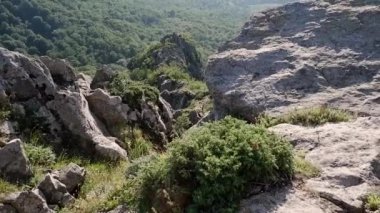 Kayalık bir dağın tepesinden yeşil yaprak döken ormana, günbatımı güneşine ve diğer dağlara güzel bir manzara..