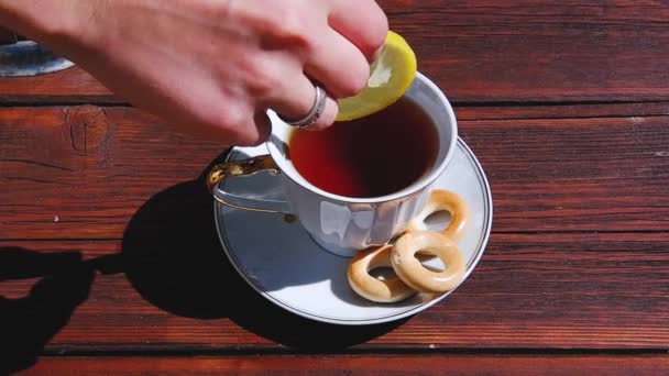 熱い紅茶にレモンのスライスを追加します 古い茶色の木製のテーブルの上に自然ティーパーティー — ストック動画