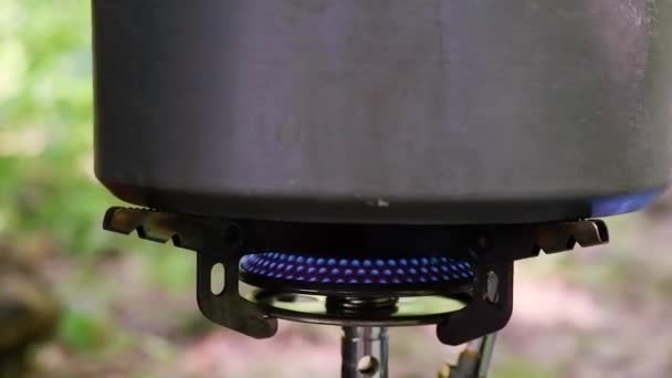 ポータブルガスバーナーの上に小さな金属製のキャンプケトルが立っています 青いガスはやかん キャンプ用品を暖める — ストック動画