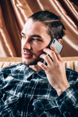 Mavi gömlekli yakışıklı genç bir adam cep telefonuyla iletişim kuruyor ve karantina sırasında evinin rahatlığıyla çalışıyor. Uzak çevrimiçi çalışma.