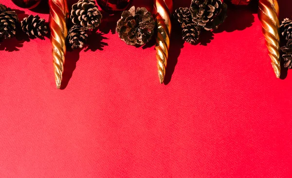 Beautiful red gradient Christmas background and lots of empty space for text. Christmas tree toys in the shape of orange icicles, red glossy shiny balls and decorative pine cones are on top.