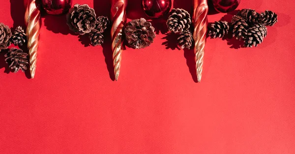 Beautiful red gradient Christmas background and lots of empty space for text. Christmas tree toys in the shape of orange icicles, red glossy shiny balls and decorative pine cones are on top.
