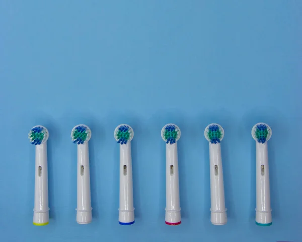 Bicos substituíveis para escova de dentes elétrica de cores diferentes no fundo azul com espaço de cópia. Deitado. Vista superior — Fotografia de Stock