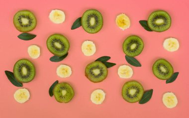 Pembe arka planda taze kivi ve muz dilimleri renkli meyve deseni. Üstten görünümden