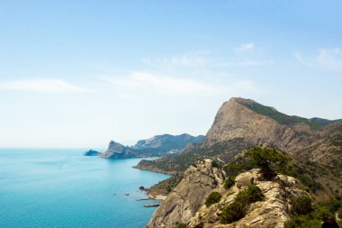 Dağların, denizin ve beyaz bulutların olduğu mavi gökyüzünün manzarası