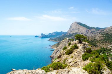 Dağların, denizin ve beyaz bulutların olduğu mavi gökyüzünün manzarası