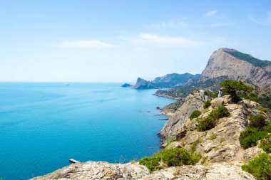 Dağların, denizin ve beyaz bulutların olduğu mavi gökyüzünün manzarası