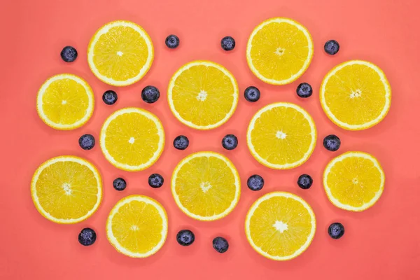 Colorful fruit pattern of fresh orange slices and blueberries on coral background
