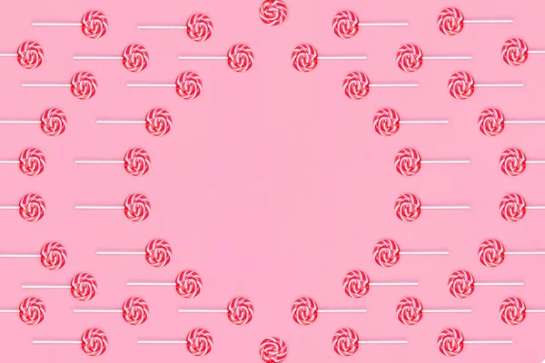 Körkocka nyalókák piros és fehér csíkokkal, rózsaszín háttérrel. — Stock Fotó
